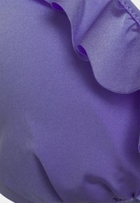 Tecido roxo com um acabamento texturizado e ligeiramente brilhante. Apresenta bordas suaves e onduladas, criando um leve franzido ao longo do tecido.