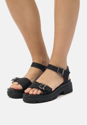 Sandalias de plataforma negras elaboradas en goma con una correa ancha y hebilla ajustable, que cuentan con una suela texturizada para un mejor agarre.