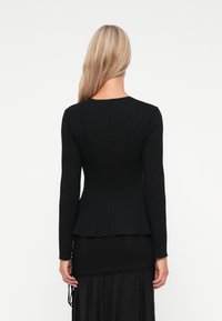Schwarzes Langarm-Oberteil mit tailliertem Oberteil, ausgestelltem Saum und subtilen Nahtdetails. Glatte Textur, hoher Halsausschnitt und einfarbig.