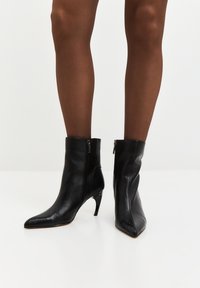 Stivaletti neri in pelle con punta affusolata, tacco alto sottile e cerniere laterali, caratterizzati da una texture liscia e un design minimalista.