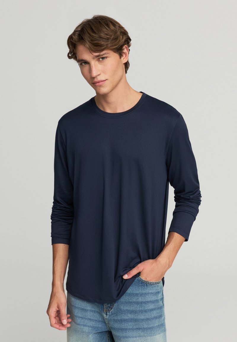 Granatowa koszulka z długim rękawem, okrągłym dekoltem, miękką teksturą i luźnym krojem, w połączeniu z jasnoniebieskimi dżinsami.