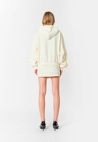 Sudadera de gran tamaño en color crema, hecha de tela suave, con capucha ajustable y puños acanalados, combinada con una falda corta a juego y tacones negros.