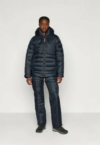 Ναυτικό μπουφάν με κουκούλα, με ραμμένες πάνελ, μπροστινό φερμουάρ και ανοιχτό καφέ λεπτομέρειες. Συνδυάζεται με αντίστοιχα θερμικά παντελόνια. Μαύρα υποδήματα.