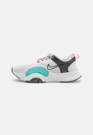 Biało-czarny sneaker Nike SuperRep z turkusowymi akcentami, wielokolorowymi sznurowadłami, nakrapianą podeszwą i pomarańczową pętelką na szarym tle.