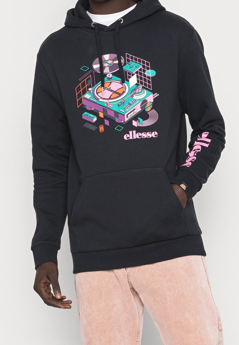 Personne portant un sweat à capuche noir avec un graphisme coloré d'une platine stylisée et le mot « ellesse » sur le devant et la manche.