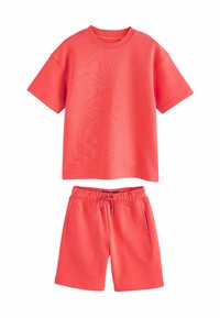 Korallfärgad träningsset som inkluderar en t-shirt med kort ärm och shorts med dragsko. Tillverkad av mjukt tyg med en slät textur och minimal detaljering.