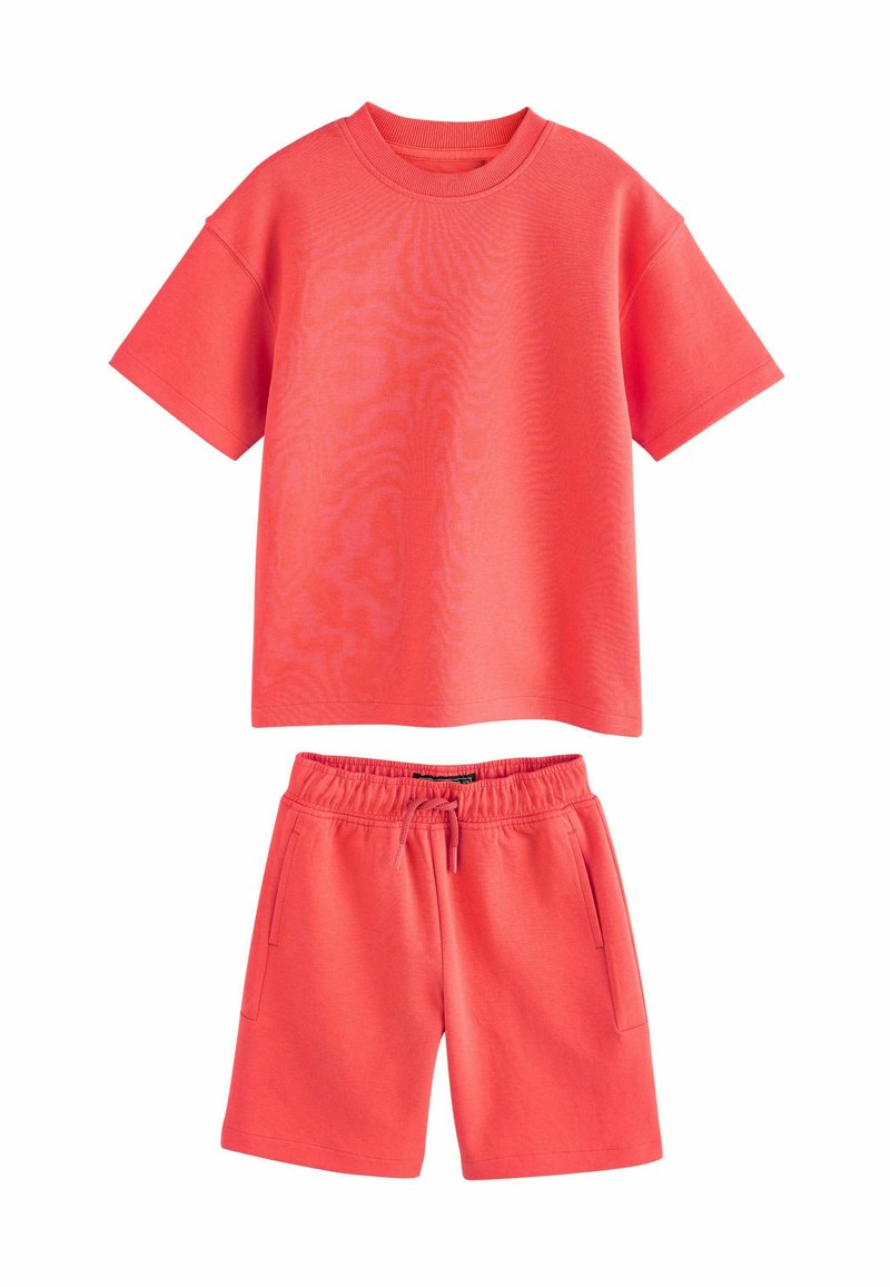Korallfärgad träningsset som inkluderar en t-shirt med kort ärm och shorts med dragsko. Tillverkad av mjukt tyg med en slät textur och minimal detaljering.
