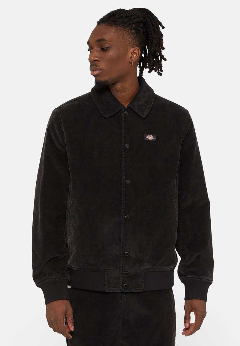 Veste en velours côtelé noire avec un col, fermeture à boutons, poignets et ourlet côtelés. Présente un petit patch de la marque sur la partie gauche de la poitrine.