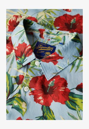 Kurzarmhemd aus hellblauem Stoff mit einem lebhaften Blumenmuster, das rote Hibiskusblüten und grüne Blätter zeigt; weiße Knöpfe und Kragen.