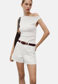 Haut blanc à épaules dénudées associé à un short en denim blanc avec un ourlet effiloché. Accessoirisé avec un sac à bandoulière tressé noir et une ceinture bourgogne.