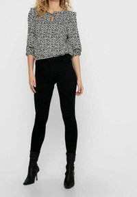 Blusa a stampa leopardata in bianco e nero con maniche a palloncino e dettaglio a occhio di chiave nel colletto, abbinata a jeans skinny neri e stivali alla caviglia.