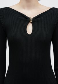 Top negru cu mâneci lungi, cu dungi, având un decolteu larg cu o decupare tip cheie, împodobită cu un detaliu sub formă de inel aurit în centrul acesteia.