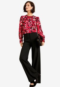 Blusa leopardata rossa e rosa con maniche a sbuffo, abbinata a pantaloni neri a vita alta e a gamba larga. Pochette nera e scarpe con tacco.