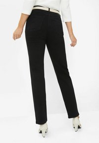 Jeans neri a gamba dritta con una texture liscia, dotati di due tasche posteriori, vita media e abbinati a scarpe con tacco di colore chiaro.