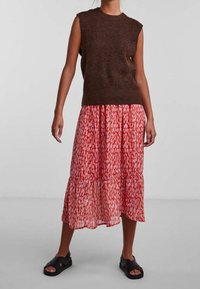 Brun ärmlös stickad topp med en röd och vit mönstrad lagad maxikjol, kompletterad med svarta slippers.