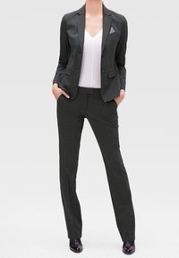 Blazer su misura grigio scuro con due bottoni, rever a punta e taschino sul petto. Abbinato a pantaloni slim-fit coordinati e scarpe nere.