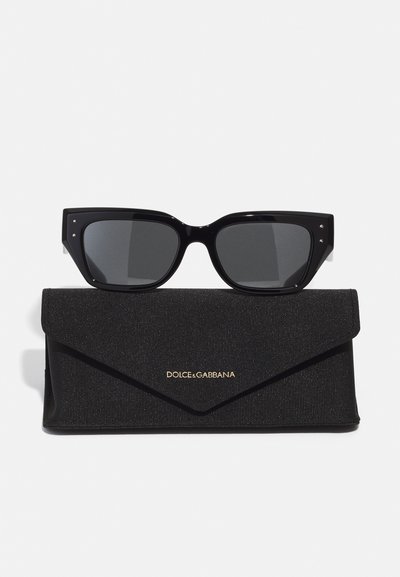 Black cat-eye sunglasses with dark lenses, featuring silver accents on corners, placed on a black textured case with gold logo.
