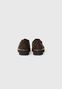 Braune Wildlederschuhe mit runder Zehenpartie, schwarzen Gummisohlen und kontrastierenden Nähten. Sauberes Design ohne zusätzliche Verzierungen.