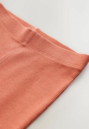 Kuparinvärinen ribbikangas, jossa on pehmeä pinta ja joustava vyötärönauha. Tarkennus istuvien legginssien yläosaan, jossa näkyy saumausyksityiskohdat.