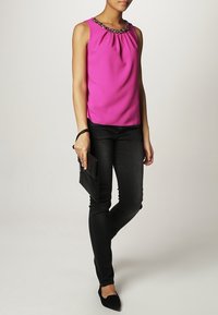 Fuchsia ärmlös topp med plisserad design och pärlbesatt halsringning, ihop med svarta skinny jeans och spetsiga svarta ballerinas, håller en svart clutch.