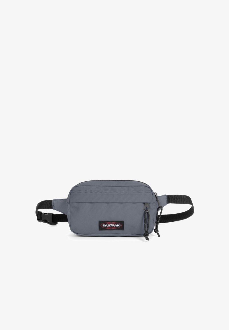 Harmaa kangastasku, jossa on suorakulmainen muoto, etuosassa vetoketjullinen tasku, säädettävä hihna ja Eastpak-logopatch. Kestävä tekstiilimateriaali.