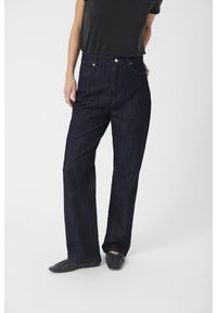 Denim jeans in dark blue with a straight leg design, high waist, front pockets, and contrasting stitch details. Paired with a black top.