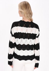 Maglione leggero a righe bianche e nere con motivo a scallop, dotato di maniche lunghe e scollatura rotonda. Tessuto testurizzato e lavorato in modo allentato.