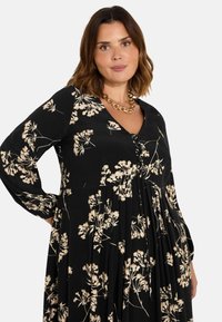 Černé květinové šaty s výstřihem do V, dlouhými rukávy a skladanou sukní. Obsahují krémové květinové vzory a detail s knoflíkem vpředu.