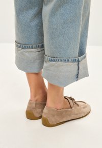 Lysbrune ruskinds loafers med rund tå, snørebånd og gummisåler, parret med oprullede lyseblå denim bukser.