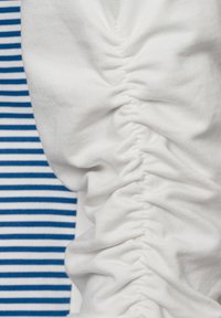 Witte stof met een geplooide textuur aan de ene kant, in contrast met blauw-witte gestreepte stof aan de andere kant. Naad zichtbaar tussen de texturen.