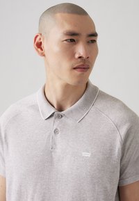 Svetlošedá polo tričko vyrobené z mäkkej látky, s golierom, dvoma gombíkmi a malým bielym logom Levi's na hrudi.