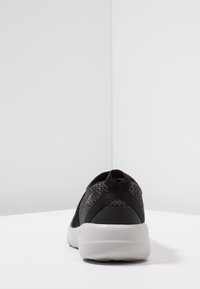 Sneaker noire avec un dessus en tricot texturé, des bandes croisées au niveau du talon et une semelle blanche et rembourrée. Fini lisse, forme arrondie.