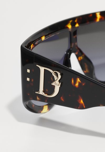 Lunettes de soleil écaille de tortue avec une épaisse monture noire, arborant un logo dor�é "D2" et des verres foncés. Texture lisse avec finition brillante.