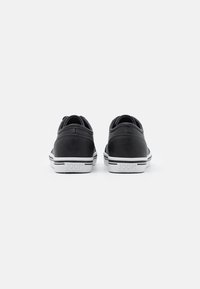 Svarte lavhals sneakers laget av skinn med perforerte paneler, hvit såle, og merkevaredetalj på hælen. Diskré stripemønster på sålen.
