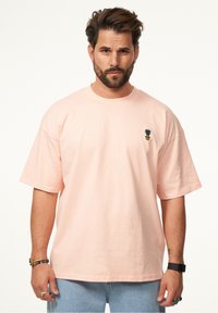 Helles rosafarbenes, übergroßes T-Shirt aus Baumwolle mit kurzen Ärmeln. Mit einem kleinen gestickten Ananas-Logo auf der linken Brust.