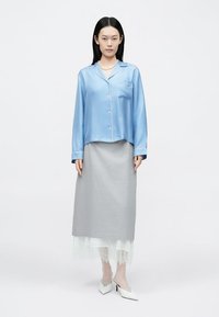 Lyseblå satengskjorte med lange ermer, grå teksturert skjørt med blonder i kanten, og hvite høyhælte sko, mot en nøytral bakgrunn.