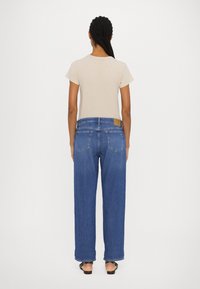 Beige T-shirt met korte mouwen, gecombineerd met hooggerokte, losse blauwe denim jeans met een patch op de achterkant van de tailleband en franjes aan de onderkant.