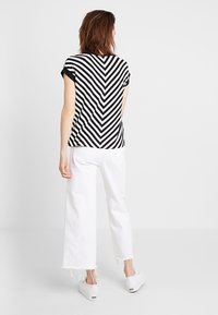 Černobílý pruhovaný top s krátkým rukávem a vzorem v chevronu, spárovaný s bílými kalhotami širokého střihu a bílými nazouvacími botami.