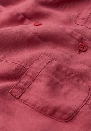 Țesătură roșie cu un buzunar dreptunghiular cusut și două nasturi roșii asortați cusute deasupra buzunarului.