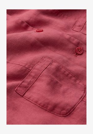 Tessuto rosso con una tasca rettangolare ricamata e due bottoni rossi abbinati cuciti sopra la tasca.