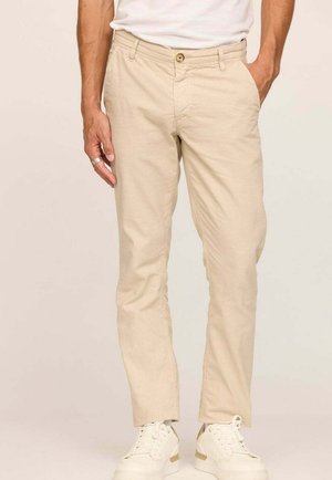 Chinos en coton beige à coupe droite, avec une fermeture à bouton, des poches latérales et une légère texture. Portés avec des baskets blanches.