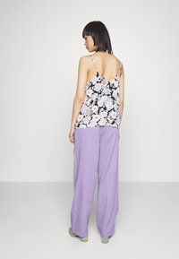 Camisola floral com alças finas em preto, roxo e branco; emparelhada com calças largas de corte solto em roxo claro; textura suave, ajuste relaxado.