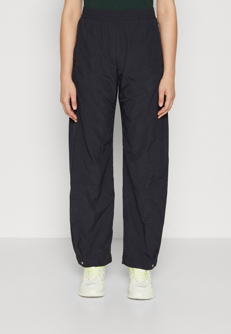 Zwarte, lichte, elastische tailleband broek met een losse fit, voorzien van twee zijzakken en een omgeslagene zoom, gecombineerd met lichtgekleurde sneakers.