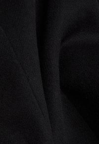 Black wool fabric with a soft texture, featuring a slightly raised surface and smooth drape, showing creases and folds.