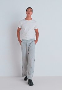 Light gray sweatpants with black side accents, paired with a fitted white t-shirt and black shoes. Smooth fabric, elastic waistband.