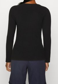 Zwarte geribbelde lange mouwen top met een ronde halslijn en een getailleerde silhouet, gecombineerd met donkere shorts. De textuur lijkt zacht en rekbaar te zijn.