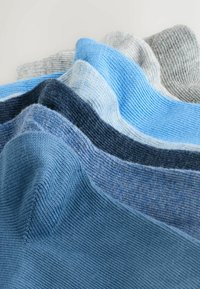 Stapeltje gebreide sokken in verschillende tinten blauw en grijs, gerangschikt in een golfpatroon op een witte achtergrond.