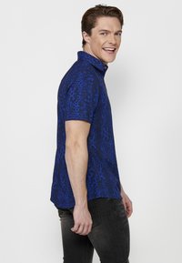 Camicia azzurra a maniche corte con un motivo testurizzato, dotata di colletto classico e bottoni, progettata con una vestibilità rilassata e orlo curvo.