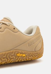 Zapatilla Merrell beige con suela de goma texturizada, que presenta un logo de Vibram, diseño de cordones y cuello acolchado para mayor comodidad.