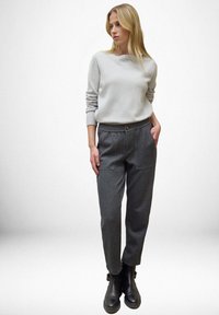 Suéter gris claro con cuello redondo y puños acanalados, combinado con pantalones gris oscuro de cintura elástica que incluyen bolsillos y un botón. Botines negros hasta el tobillo.